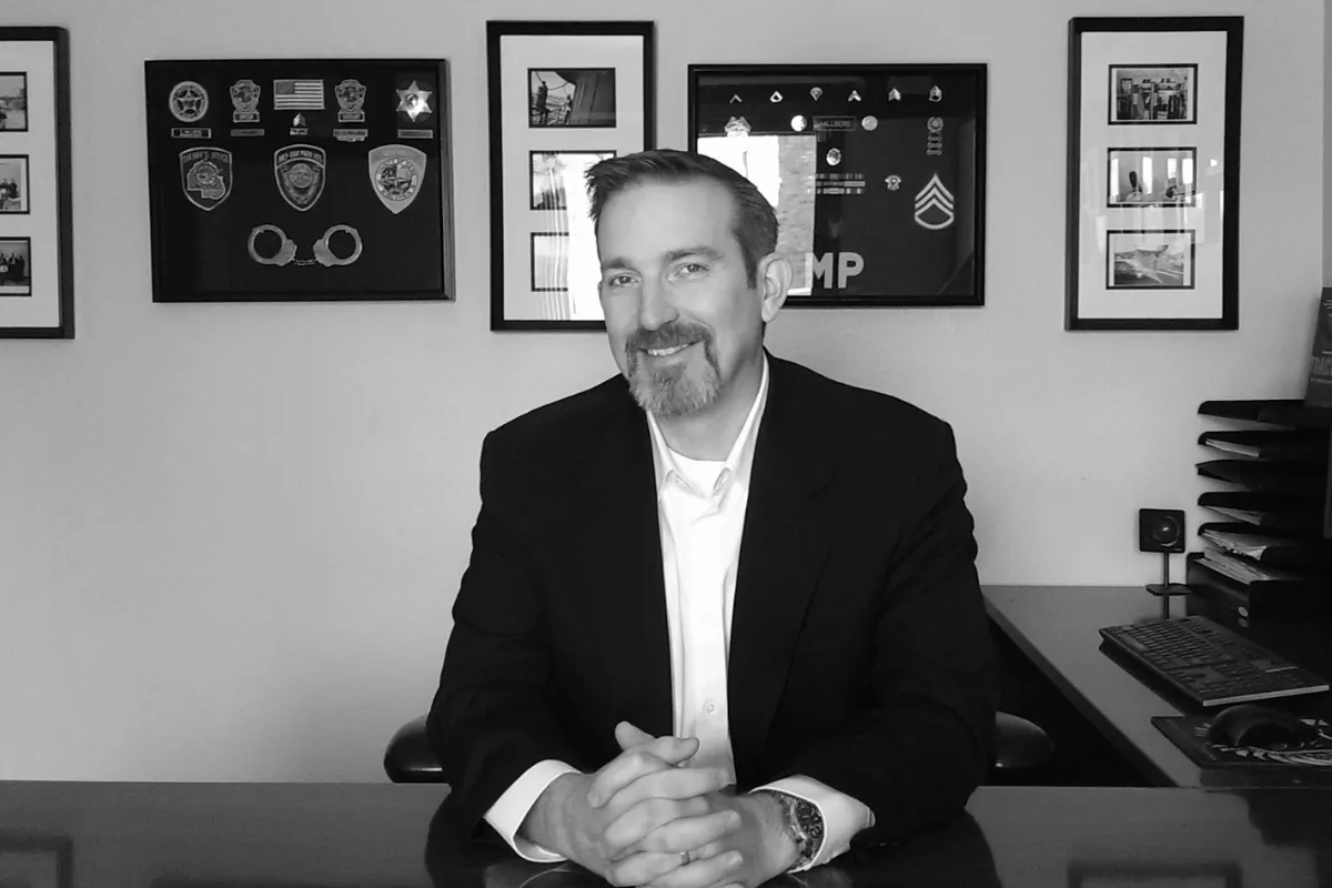 Chris Hallberg at his desk with military and law enforcement badges behind him