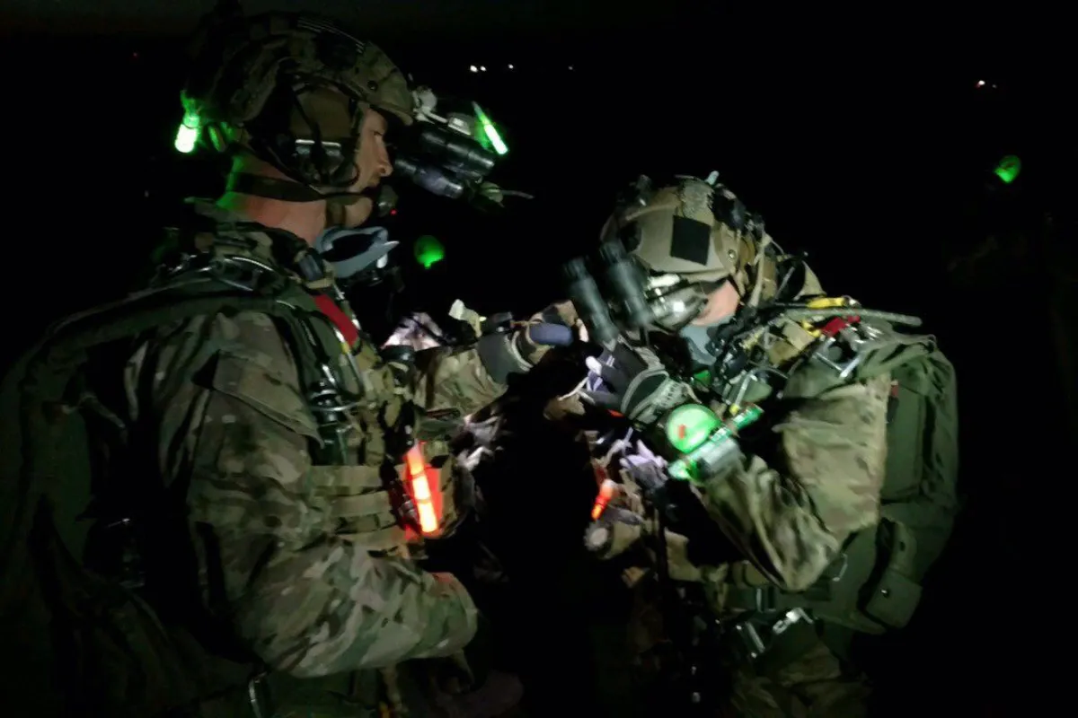 Two Special Operations soldiers conferring over a weapon under night vision light